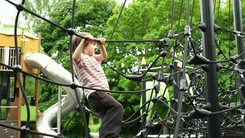 A child boy is climbing up an alpine grid in a park on a playground on a hot Stock Footage 312515510
