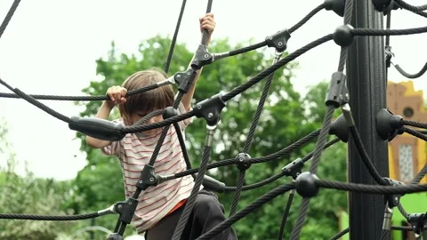 A child boy is climbing up an alpine grid in a park on a playground on a hot Stock Footage 312515806