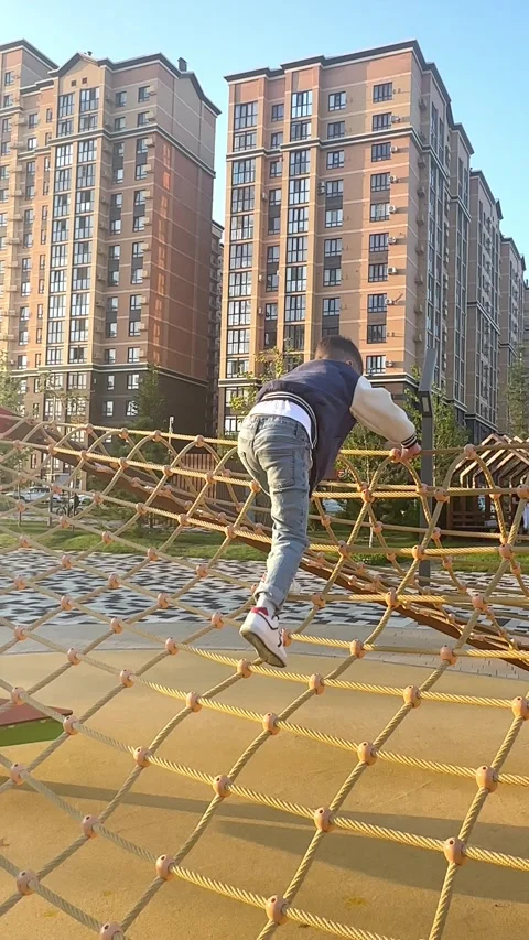 A child boy climbs up an alpine grid in a park on a playground on a hot summer Stock Footage 307040457