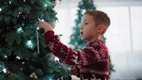 Child boy decorates a Christmas tree by hanging ornaments Video stock 257563641