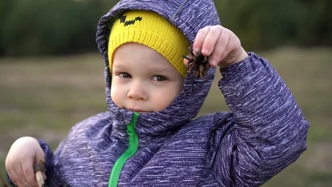 A child / boy dressed in an autumn jacket and hood holds a lump in his hand 스톡 동영상 127768012