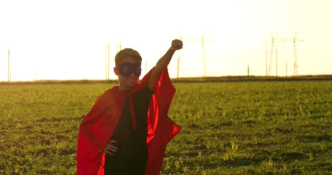 Child boy dressed as superhero stands confidently in field. Bright sunset Stock Footage 336186064