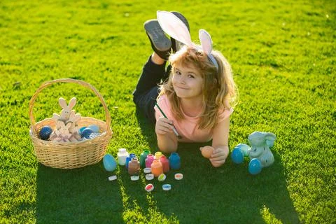 Child boy with easter eggs and bunny ears outdoor painting eggs. Cute kid having Stock Photos