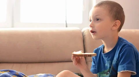 Child (boy) eats bread with butter and watchs TV Video stock 39479277