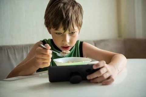 Child boy eats by game. Kid eating and surfing on internet or playing vide... Stock Photos