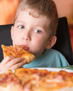 Child boy eats pizza sitting at the table Stock Photos