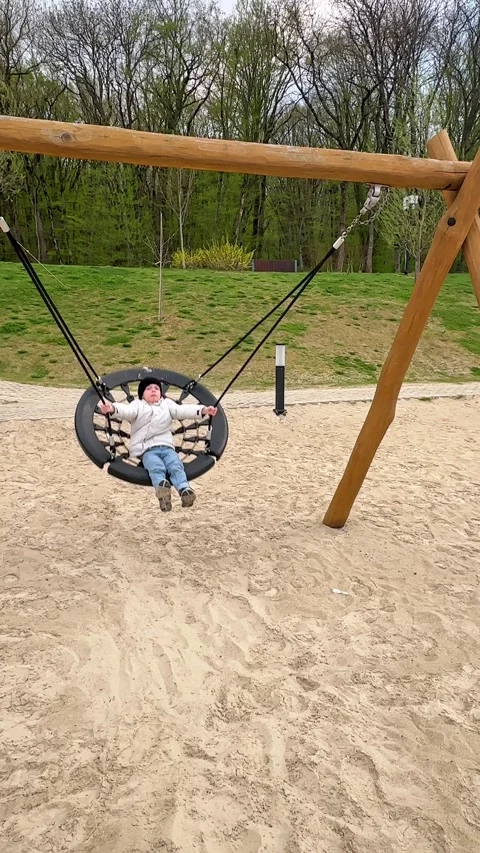 Child boy enjoys swinging on a round swing at a playground with sandy ground Stock Footage 340652986