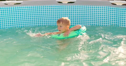 Child boy has fun in backyard pool, splashing happily on inflatable lap Stock Footage 254424601