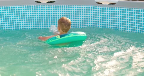 Child boy has fun in backyard pool, splashing happily on inflatable lap Stock Footage 254592981