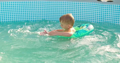 Child boy has fun in backyard pool, splashing happily on inflatable lap Stock Footage 254978900