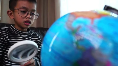 Child boy inspecting a model of the earth with a magnifying glass at home Stock Footage 246183871