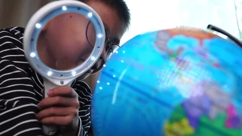 Child boy inspecting a model of the earth with a magnifying glass at home Stock Footage 246183937