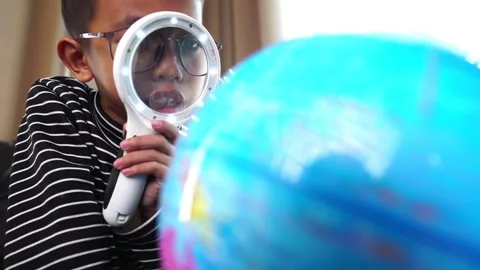 Child boy inspecting a model of the earth with a magnifying glass at home Stock Footage 246184436