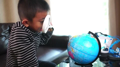 Child boy inspecting a model of the earth with a magnifying glass at home Stock Footage 246184517