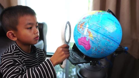 Child boy inspecting a model of the earth with a magnifying glass at home Stock Footage 246184728