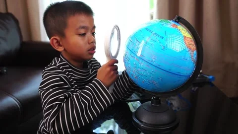 Child boy inspecting a model of the earth with a magnifying glass at home Stock Footage 246184898