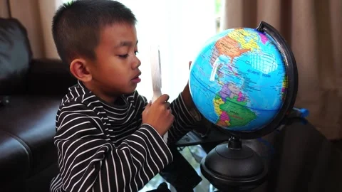 Child boy inspecting a model of the earth with a magnifying glass at home Stock Footage 246184925