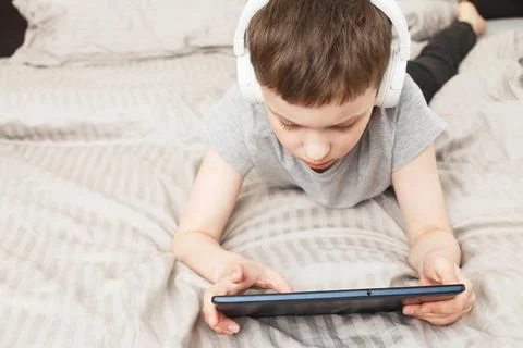 Child boy lying on bed with pc tablet with wireless headphones Stock-Fotos