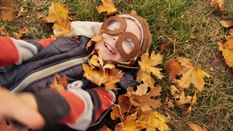Child boy lying on ground and catching falling yellow golden leaves. Stock Footage 230565362