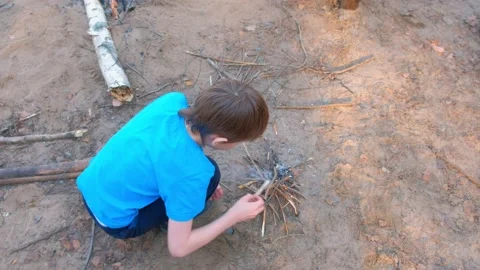 Child boy making bonfire from firewoods branches nature sitting near it. Stock Footage 136422947