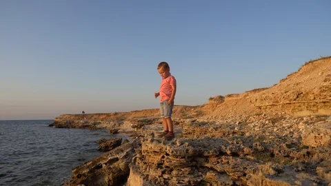 Child boy pick up a stone and throw it in a sea . Boy on a sky, sea background Stock Footage 114317003