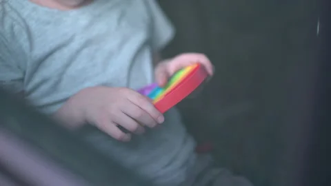 Child boy playing with rainbow popit or simple dimple in car. Modern silicone Stock Footage 156210163