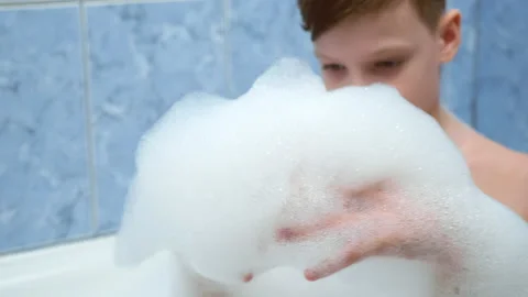 Child boy is playing with white foam sitting in bath at home, water games. 스톡 동영상 153762344