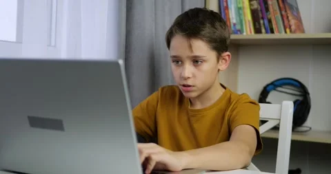 Child boy plays computer game on laptop at home. Child focuses on screen and Stock Footage 330860918