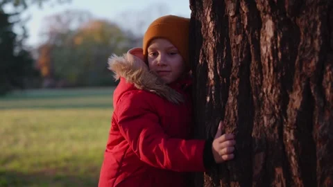 Child boy in a red jacket, leaning against a tree trunk Stock Footage 292918123