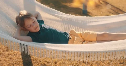 Child boy is resting in hammock in garden, in sunny summer day. Stock Footage 177991037