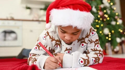 Child boy in a santa hat lying on a plaid smiles dreamily and writes a letter to Stock Footage 219383946