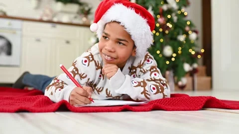 Child boy in a santa hat lying on a plaid smiles dreamily and writes a letter to Stock-Footage 221415013