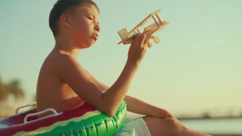 Child boy sitting alone on sandy beach on sea coast and playing with toy plane Stock Footage 317897777