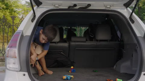Child boy sitting in the open trunk of a car while relaxing on a trip. The Stock Footage 249960274