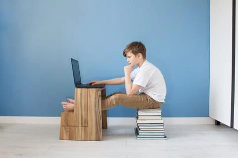 Child boy sitting on stack of books typing on his laptop, studying online at Stock Photos