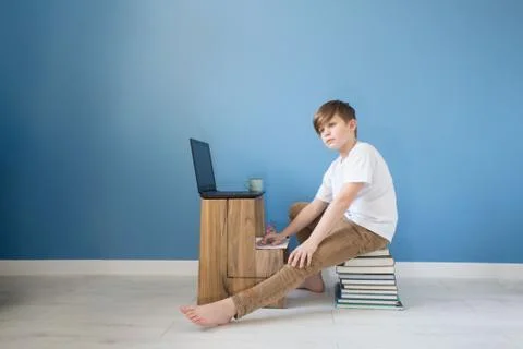 Child boy sitting on stack of books with his laptop, studying online at home, Stock Photos