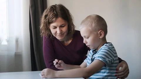Child boy sitting at the table at home and drawing together with their mom Stock Footage 120434240