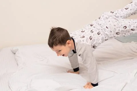 Child boy standing upside down and showing tongue on his bed at the morning Stock Photos