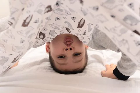 Child boy standing upside down and showing tongue on his bed at the morning 写真素材