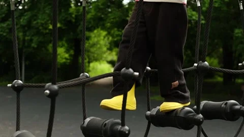 A child boy is stepping up an alpine grid in a park on a playground on a hot Vídeos de archivo 312515262