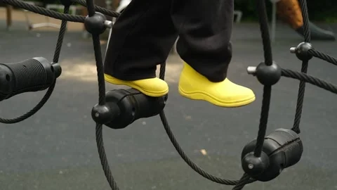 A child boy is stepping up an alpine grid in a park on a playground on a hot Stock Footage 312515582