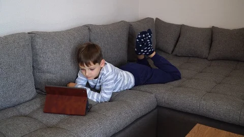 The child boy with tablet pc lies on the couch and studies online. Cute Stock Footage 128983059