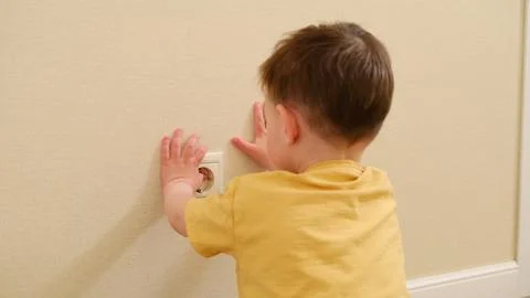 Child boy touching electric socket on wall. Dangerous behavior at home. Dom.. Stock Photos