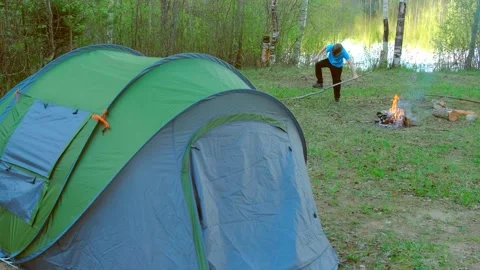 Child boy is trying to break branch for bonfire near tent on bank of lake. Stock-Footage 136022643