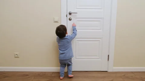 Child boy trying to open white door by reaching for metal handle. Curious Stock Footage 342277916