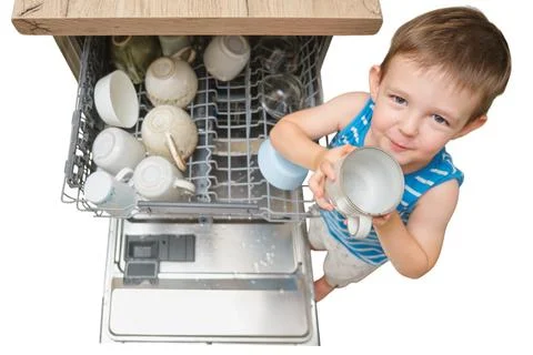 Child boy unloading dishwasher in kitchen. Little helper putting cup into rac Stock Photos