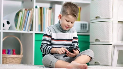 A child boy is using his smartphone while sitting on the carpet at home Vidéo 102818835