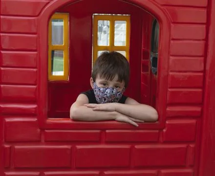 Child boy using a mask on a red wall looking to the camera 스톡 사진