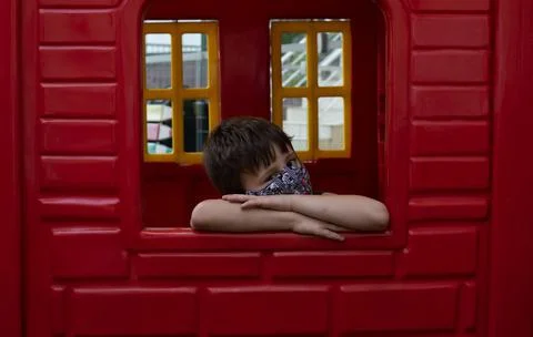 Child boy using a mask on a red wall looking to the camera Foto stock