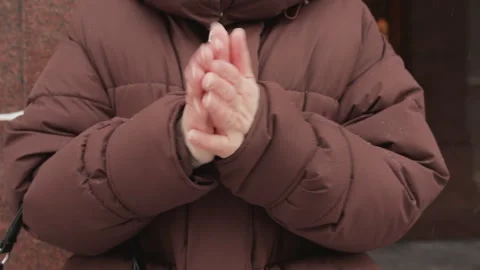 Child in brown puffer jacket rubbing hands for warmth beside cold outdoor wall Stock Footage 345666330